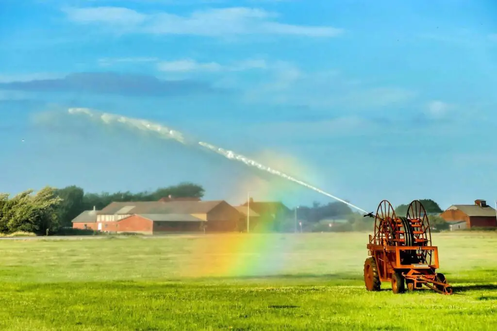 An overhead irrigation system watering the green grass near a house